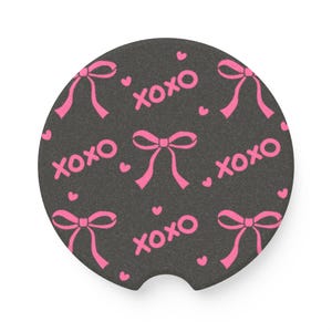 May include: A black round coaster with a pink and white pattern of bows and the text "xoxo".