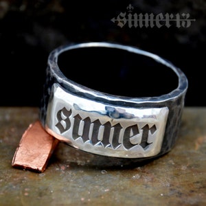 May include: A silver ring with a hammered finish and a rectangular plaque engraved with the word "Summer" in a gothic font.