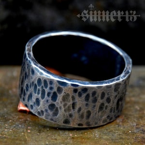 May include: A wide silver band ring with a hammered texture. The ring has a dark, almost black, oxidised finish.