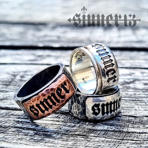 May include: Three silver rings with the word "Summer" engraved on each. The rings are stacked on top of each other. The top ring is smooth, the middle ring has a hammered texture, and the bottom ring has a textured surface.