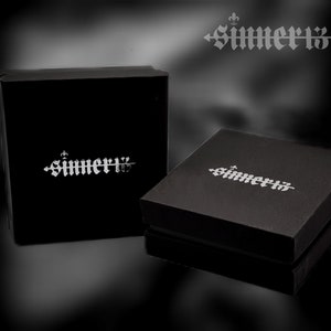 May include: Two black boxes with the word "SIMMER13" printed in silver on the top. The boxes are on a black background.