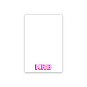 May include: A white card with the letters "KRB" in pink with a red outline.