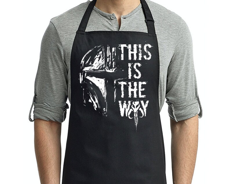 May include: Black apron with a white graphic of a Mandalorian helmet and the text "This is the Way".