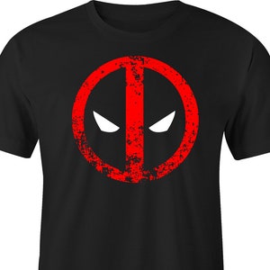 May include: Black t-shirt featuring a distressed red graphic of a circle with a vertical line and two white eye shapes. The design is reminiscent of a comic book character's emblem. The shirt is made of a soft material.