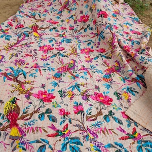 May include: A beige kantha quilt with a floral and bird print. The quilt features pink, blue, yellow, and green colours. The quilt is hand-stitched and has a traditional Indian design.