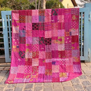 May include: A rectangular patchwork quilt featuring a variety of pink and magenta fabric squares with diverse floral, geometric, and abstract patterns. The quilt displays visible running stitch details throughout and includes the text Ganeshexport.