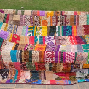 May include: A large rectangular quilt featuring a patchwork of various fabric strips in diverse colors including yellow, red, blue, green, and purple. The textile displays intricate patterns, floral motifs, and geometric designs with visible running stitch details throughout.