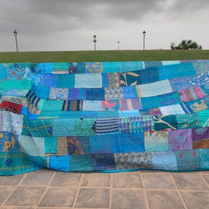 May include: A rectangular patchwork quilt featuring a variety of blue, teal, and turquoise fabric squares. The quilt displays diverse patterns including floral, geometric, and abstract prints, all joined together with visible running stitch detailing.