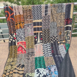 May include: A black kantha quilt with a patchwork design featuring various colors and patterns, including brown, gold, green, and red. The quilt is made of cotton and is hand-stitched.