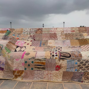 May include: A large rectangular quilt constructed from numerous patchwork fabric squares featuring a variety of printed patterns including floral, geometric, and polka dot designs in muted earth tones, beige, and cream with visible running stitch details.