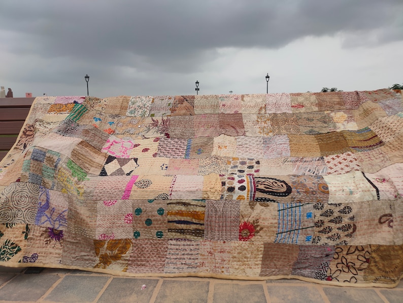 May include: A large rectangular quilt constructed from numerous patchwork fabric squares featuring a variety of printed patterns including floral, geometric, and polka dot designs in muted earth tones, beige, and cream with visible running stitch details.
