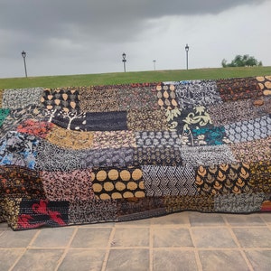 May include: A rectangular patchwork quilt featuring a variety of fabric squares with diverse patterns in black, white, gold, and red. The textile displays intricate kantha stitching throughout, creating a textured surface with repeating geometric, floral, and abstract motifs.