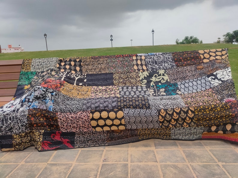 May include: A rectangular patchwork quilt featuring a variety of fabric squares with diverse patterns in black, white, gold, and red. The textile displays intricate kantha stitching throughout, creating a textured surface with repeating geometric, floral, and abstract motifs.