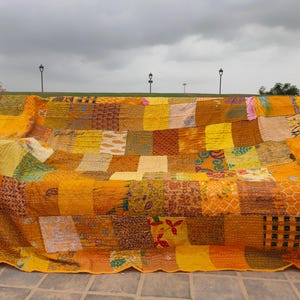 May include: A rectangular patchwork quilt featuring a variety of yellow, gold, and orange fabric squares. The quilt displays diverse patterns including floral, geometric, and paisley prints, all joined together with visible running stitch embroidery.