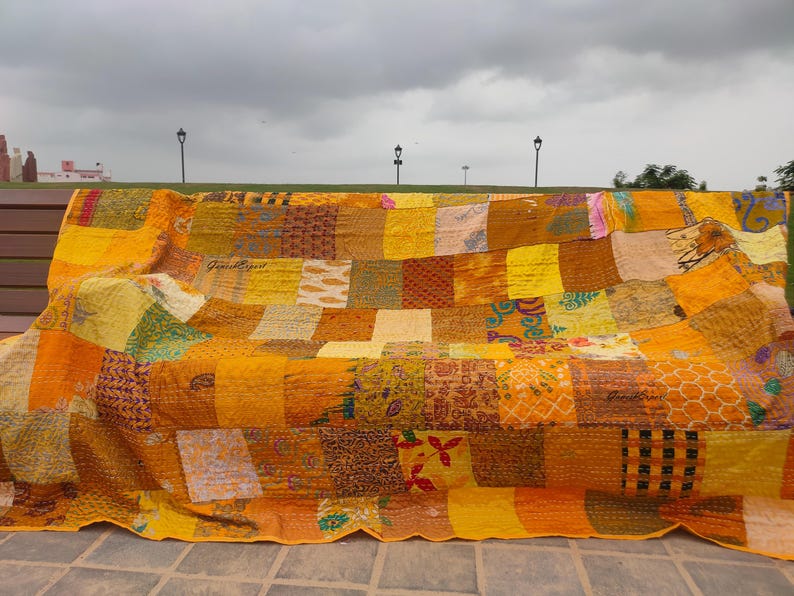 May include: A rectangular patchwork quilt featuring a variety of yellow, gold, and orange fabric squares. The quilt displays diverse patterns including floral, geometric, and paisley prints, all joined together with visible running stitch embroidery.