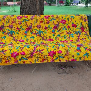 May include: A yellow kantha quilt with a floral and bird pattern. The quilt is draped over a bench in an outdoor setting.