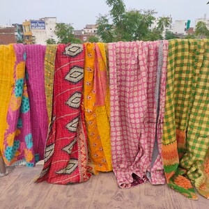 May include: A collection of colorful kantha quilts hanging on a clothesline. The quilts are made of patchwork fabric and have a variety of patterns, including floral, geometric, and plaid.