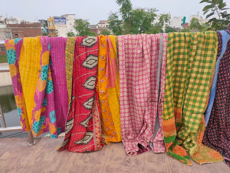 May include: A collection of colorful kantha quilts hanging on a clothesline. The quilts are made of patchwork fabric and have a variety of patterns, including floral, geometric, and plaid.