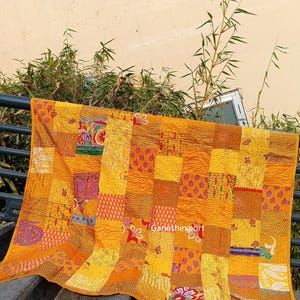 Op de afbeelding: Een rechthoekige patchwork quilt met een felgele basis van diverse aan elkaar genaaide stoffen vierkanten. De quilt toont diverse bloemmotieven, geometrische en abstracte patronen in tinten oranje, rood, groen en paars. De tekst Ganeshexport is zichtbaar.