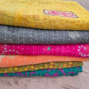 May include: A stack of six kantha quilts in various colors and patterns, including yellow, gray, pink, orange, green, and purple. The quilts are made of recycled saris and are hand-stitched.