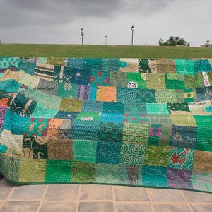 May include: A large rectangular quilt featuring a patchwork design composed of numerous fabric squares in various shades of green, teal, and blue. The quilt displays a variety of printed patterns, including floral, geometric, and abstract motifs.
