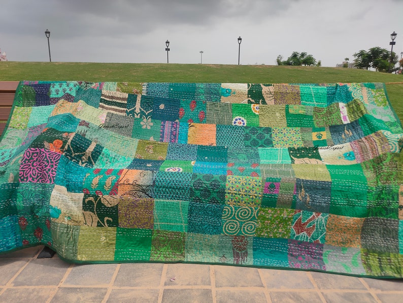 May include: A large rectangular quilt featuring a patchwork design composed of numerous fabric squares in various shades of green, teal, and blue. The quilt displays a variety of printed patterns, including floral, geometric, and abstract motifs.
