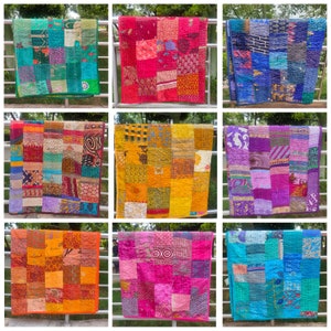 May include: Nine colourful patchwork quilts hanging on a metal fence. The quilts are made of various fabrics in shades of blue, green, purple, pink, orange, and yellow. Each quilt has a unique pattern and design.