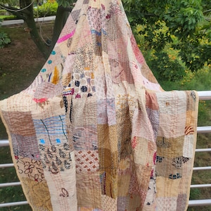 May include: A patchwork quilt made from various fabrics in shades of brown, beige, and cream. The quilt is hand-stitched and has a rustic, vintage look.