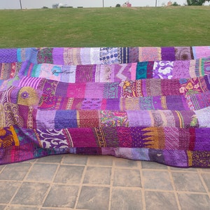 May include: A rectangular patchwork quilt featuring a variety of purple fabric panels with diverse floral, geometric, and paisley patterns. The textile displays visible running stitch details throughout and includes the text GaneshExpert printed twice.