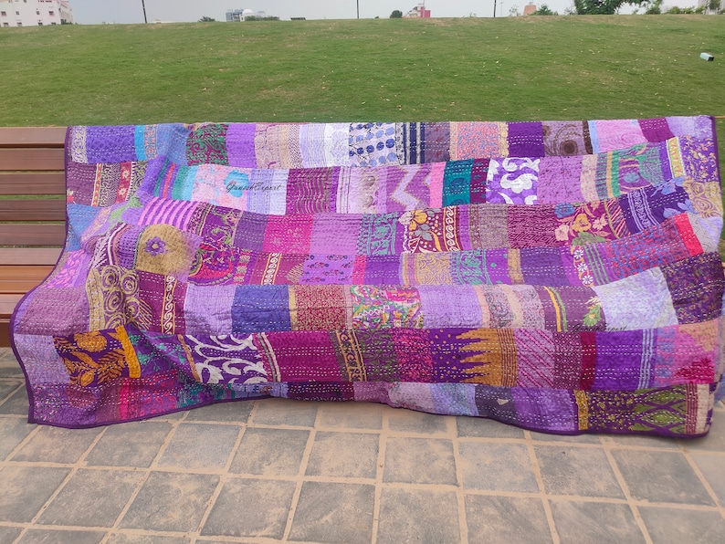 May include: A rectangular patchwork quilt featuring a variety of purple fabric panels with diverse floral, geometric, and paisley patterns. The textile displays visible running stitch details throughout and includes the text GaneshExpert printed twice.
