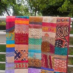 May include: A colorful patchwork quilt made from recycled saris. The quilt is made up of squares of different fabrics, each with a unique pattern. The quilt is a vibrant mix of colors, including red, orange, yellow, green, blue, and purple.