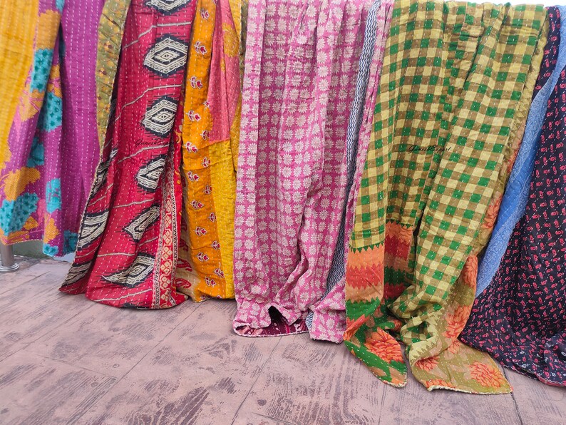 May include: A collection of colourful kantha quilts with various patterns, including floral, geometric and plaid designs. The quilts are made from recycled saris and are hand-stitched.