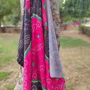 May include: A pink, black and blue kantha quilt with a floral pattern. The quilt is draped over a tree trunk.