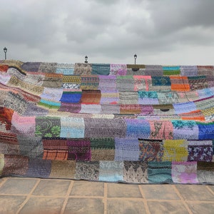 May include: A large rectangular patchwork quilt constructed from numerous small fabric squares in a wide variety of colors, patterns, and textures. The quilt features visible running stitch embroidery throughout and is finished with a grey border.