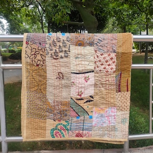 Könnte beinhalten: Eine rechteckige Patchwork-Decke aus verschiedenen Stoffquadraten mit unterschiedlichen Mustern, darunter florale, geometrische und abstrakte Drucke in Beige-, Braun-, Cremetönen und bunten Akzenten, zusammengehalten durch sichtbare Steppstiche.