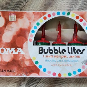 Puede incluir: Caja vintage de NOMA Bubble Lites. Presenta un fondo rojo y blanco con el logotipo de NOMA y el texto "Bubble Lites". Contiene siete luces individuales con bombillas rojas y bases verdes. La caja dice "All American Made".