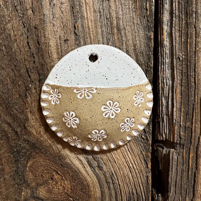 Pu&ograve; includere: Una tasca da parete in ceramica fatta a mano a forma di mezza luna. La met&agrave; superiore &egrave; bianca macchiettata e la met&agrave; inferiore &egrave; beige con motivi floreali bianchi. Il bordo &egrave; smerlato e c'&egrave; un foro nella parte superiore per appenderla.