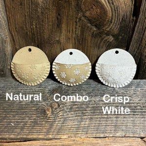 Pu&ograve; includere: Tre fioriere da parete in ceramica nei colori naturale, combo e bianco brillante. Ogni fioriera &egrave; rotonda con una tasca a semicerchio, ornata da motivi floreali e un bordo smerlato. Le fioriere hanno un foro nella parte superiore per essere appese. Le parole "Natural", "Combo" e "Crisp White" sono sotto.