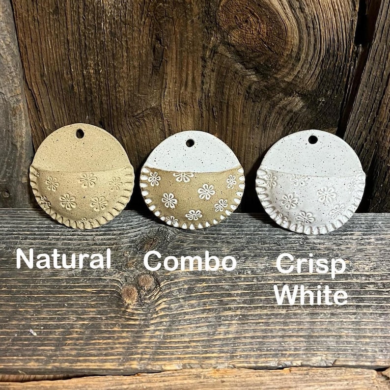 Pu&ograve; includere: Tre fioriere da parete in ceramica nei colori naturale, combo e bianco brillante. Ogni fioriera &egrave; rotonda con una tasca a semicerchio, ornata da motivi floreali e un bordo smerlato. Le fioriere hanno un foro nella parte superiore per essere appese. Le parole "Natural", "Combo" e "Crisp White" sono sotto.