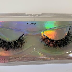 May include: A pair of black false eyelashes in a clear plastic case. The case has a holographic background with the text "M100-P". The eyelashes are long and full, designed to enhance the eyes.