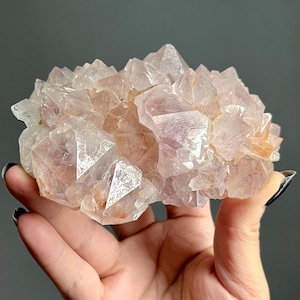 May include: A cluster of translucent, pale pinkish-purple quartz crystals with sharp, multifaceted points. The mineral specimen features a dense arrangement of jagged, crystalline structures with varying levels of clarity and light-reflecting surfaces.