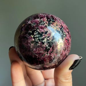 Peut inclure: Une pierre pr&eacute;cieuse sph&eacute;rique polie, m&eacute;langeant des teintes bordeaux fonc&eacute;, noires et vertes. La surface de l'orbite refl&egrave;te la lumi&egrave;re, r&eacute;v&eacute;lant ses motifs et textures naturels. Cette sph&egrave;re d&eacute;corative est un objet de d&eacute;coration unique.