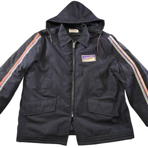 May include: A dark navy blue zip-up jacket with a hood, featuring a rectangular patch on the chest that reads Federal Express. The sleeves have vertical stripes in orange, white, and purple. The jacket includes two front pockets and a collar.