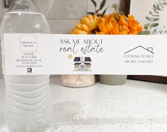 May include: A white water bottle with a label that says "Ask Me About Real Estate". The label also has a cartoon house and the text "Looking to buy or sell a home?"