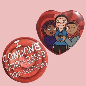 May include: Two red pinback buttons. One is round with the text "I CONDONE WORM BASED BODY-SNATCHING". The other is heart-shaped, featuring three cartoon figures making a heart shape with their hands.