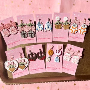 May include: A collection of handmade polymer clay earrings featuring characters from Star Wars. The earrings are displayed on pink cards with the text "Sweet Love Clay".