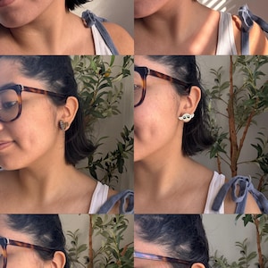 Puede incluir: Una mujer con gafas y un top blanco sin mangas lleva una variedad de peque&ntilde;os pendientes. Los pendientes tienen forma de robot, hoja y media luna.