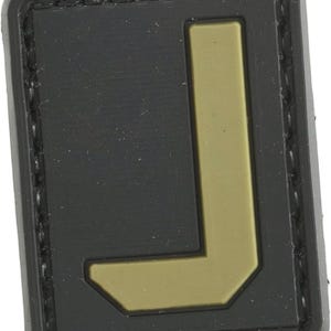 May include: Black patch with a tan letter L in the center. The patch has a stitched border.