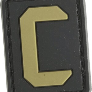 May include: A black and tan velcro patch with the letter "C" in a bold, blocky font.