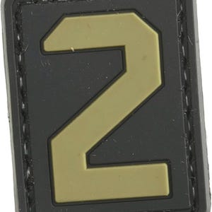 Puede incluir: Un parche de velcro negro y marrón con el número "2" en una fuente grande y en negrita.